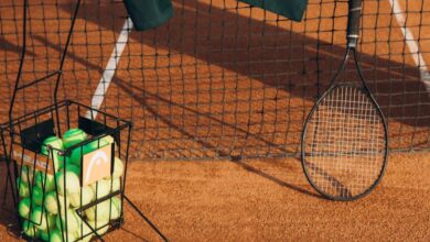 Sports Enthusiast - Tennis racket and balls with net on a clay court, captured in bright daylight.