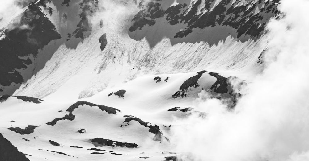 Winter Climbing - Black and white photo of snow-covered alpine mountains enveloped in clouds, creating a dramatic serene atmosphere.