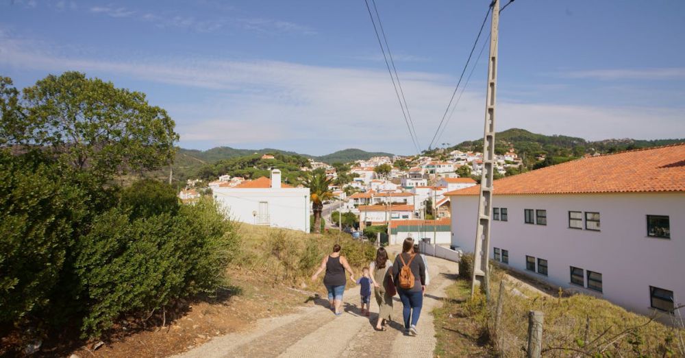 Group Adventures - Family walking along a scenic path in a picturesque village surrounded by hills.