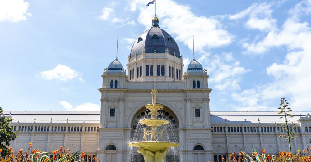 One-Day Garden Tour - Exterior view of the Royal Exhibition Building in Melbourne with a clear blue sky and vibrant garden.