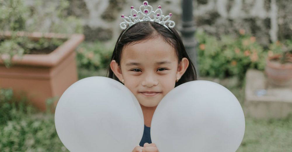 Outdoor Garden Events - A joyful young girl wearing a tiara, holding balloons in an outdoor setting.