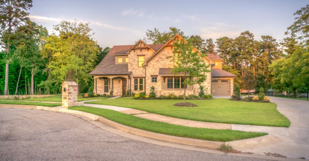 Private Garden Tours - Elegant stone family home with manicured lawn, trees, and driveway on a sunny day.