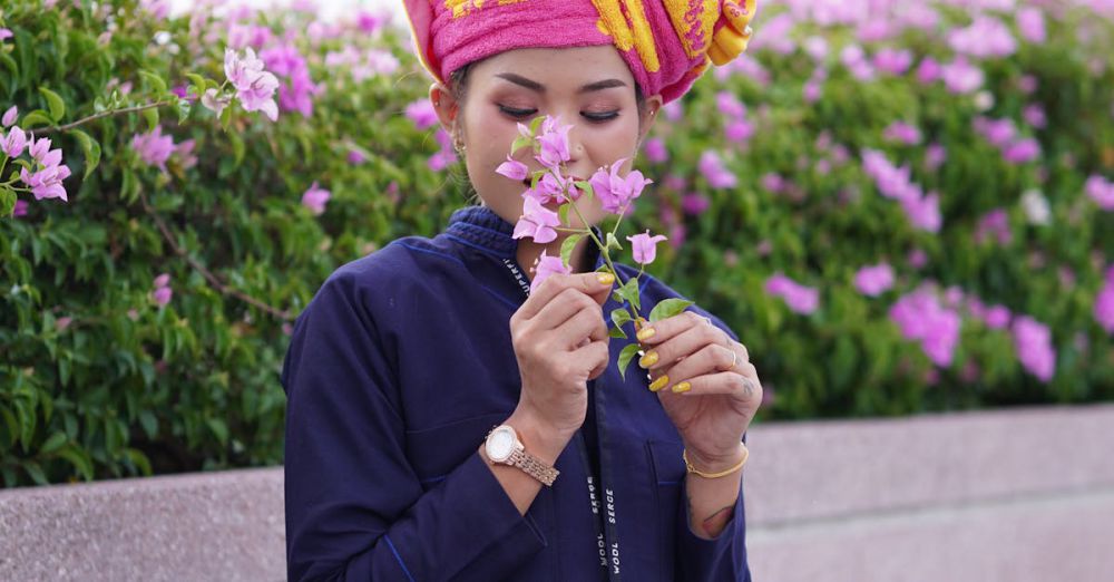 Aromatherapy Gardens - An Asian woman in traditional attire smells flowers while sitting on a bench outdoors.