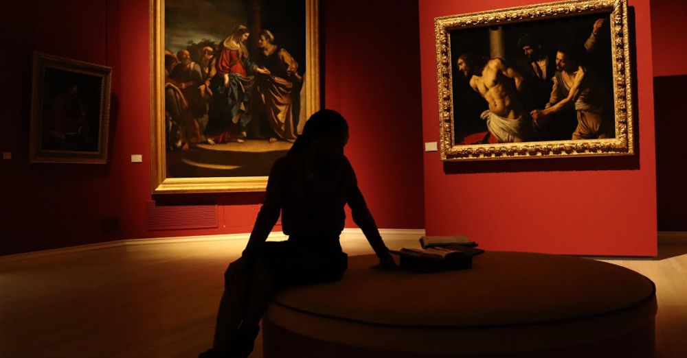 Museum Experience - Silhouetted visitor in an art gallery with dramatic lighting on classic paintings.