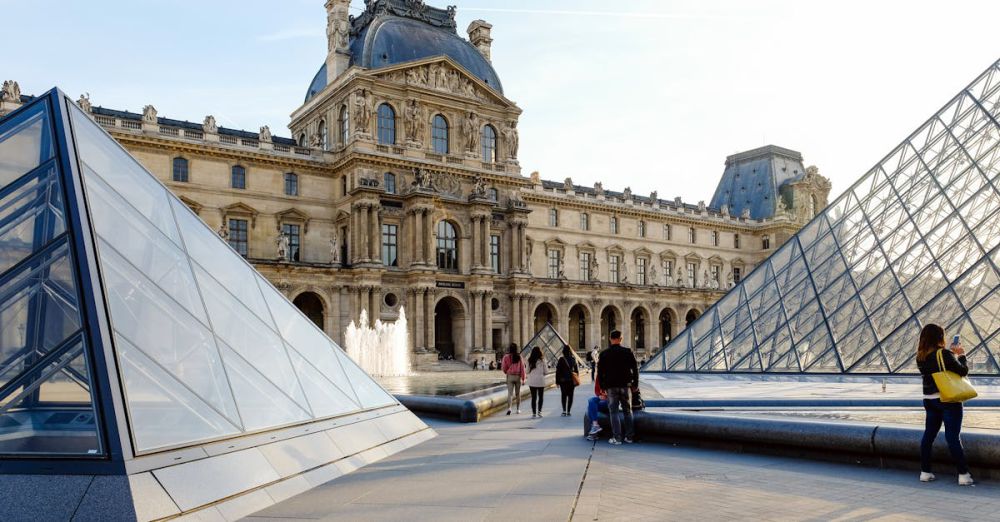 Museum Tour Tips - The Louvre Museum and its glass pyramids in Paris, bustling with tourists on a sunny day.