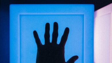 Interactive Museums - Silhouette of a hand reaching toward a glowing blue backlit modern art installation.