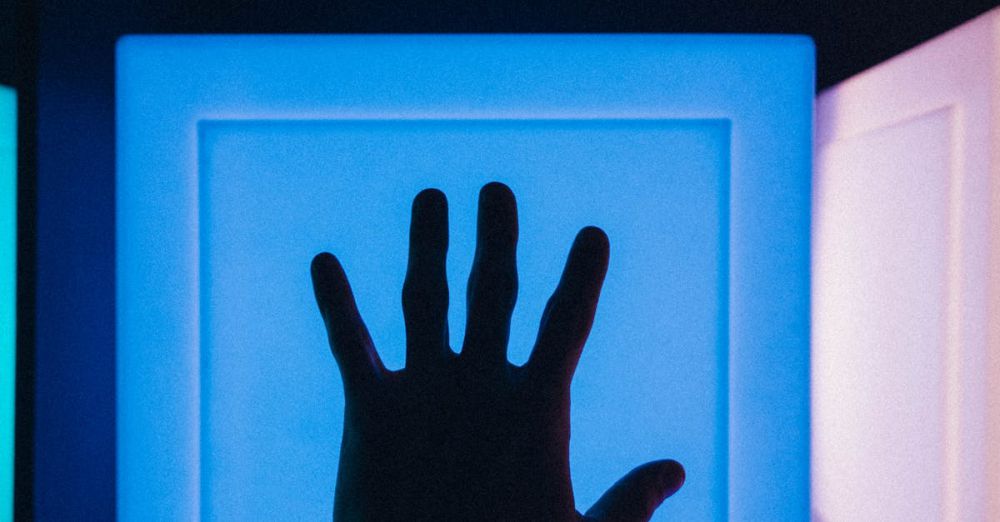 Interactive Museums - Silhouette of a hand reaching toward a glowing blue backlit modern art installation.