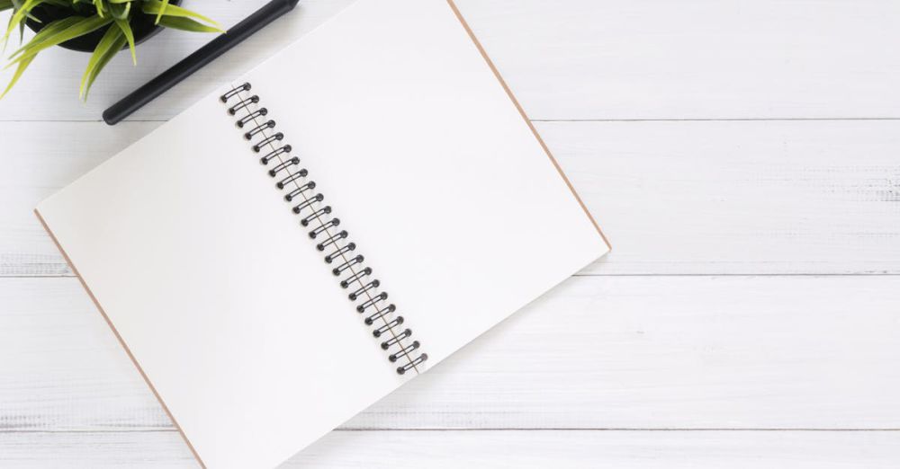 Planning - Open spiral notebook on white desk with black pen and green plant. Ideal for planning.