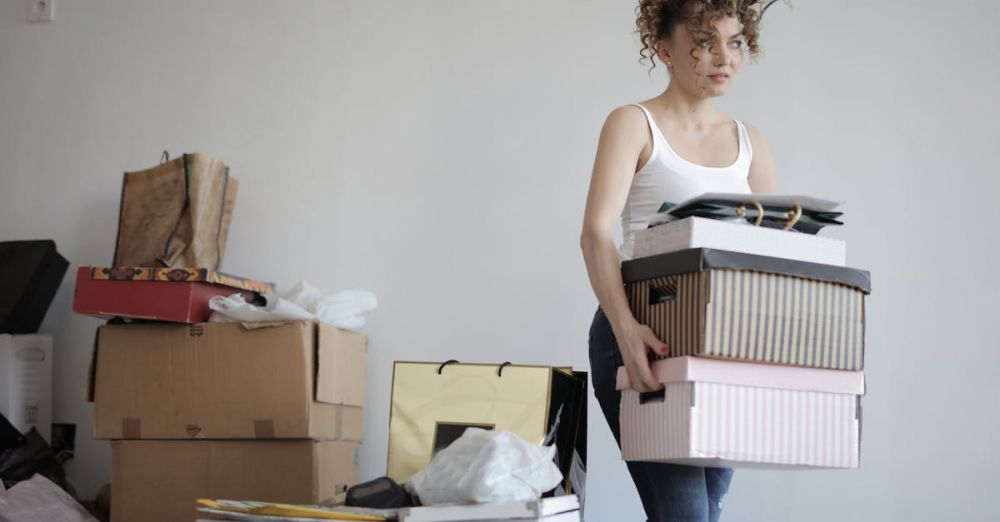 Packing - A young woman carrying boxes during a move into a new apartment, surrounded by packed belongings.