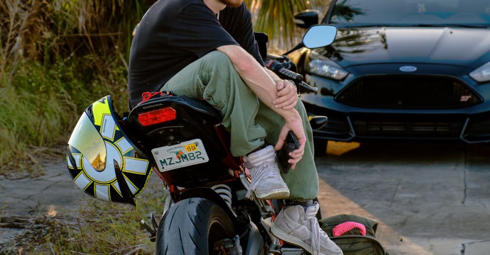 Relaxing Road Trips - Man sitting on a motorcycle next to a car, enjoying a sunny day scene.