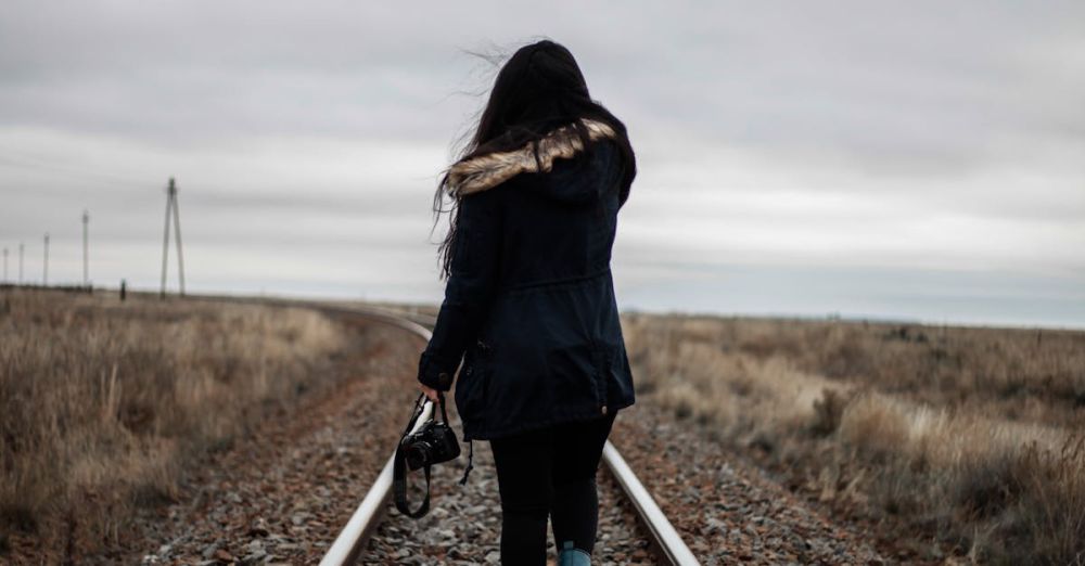 Solo Road Trips - Rear view of a woman walking alone on railway tracks during twilight, conveying solitude and journey.