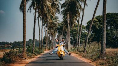 Couple Road Trips - A joyful couple rides a yellow scooter through a scenic palm-lined road, capturing the essence of tropical travel and adventure.