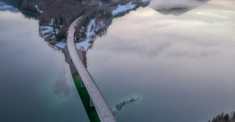 Mountain Road Trips - A stunning aerial view of a bridge over a lake surrounded by Alps in Bavaria, Germany.