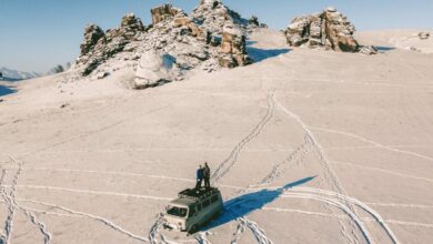 Winter Road Trip - Drone captures people on a van amid a snow-covered mountain landscape in winter.