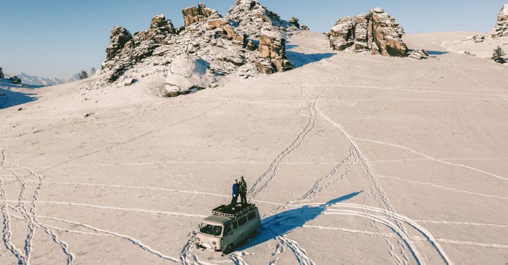 Winter Road Trip - Drone captures people on a van amid a snow-covered mountain landscape in winter.