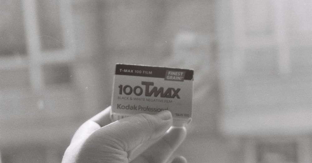 Beginner Photography - Close-up of Kodak T-Max 100 black and white film held by a hand, showcasing vintage photography equipment.