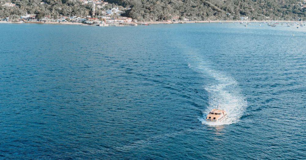 Photography Tour Choice - Aerial view of a lonely boat navigating the vast blue ocean towards a scenic coast.