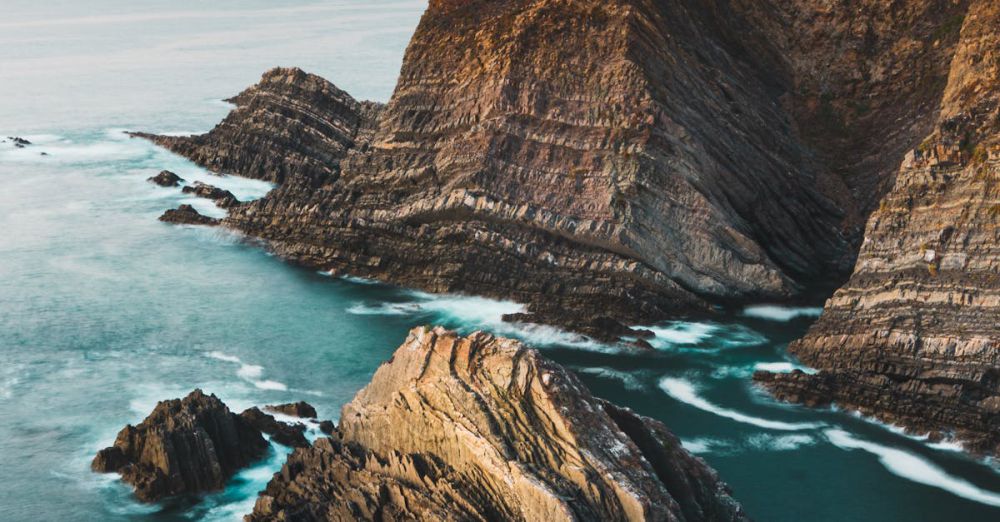 Landscape Photography - A breathtaking view of rugged cliffs and ocean waves in Beja District, Portugal during a serene sunset.