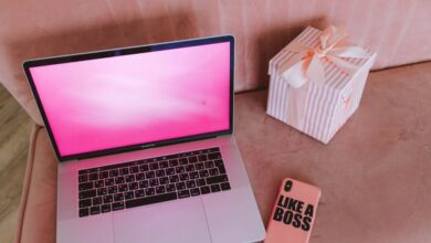 Tech Gifts - A modern workspace featuring a pink-themed laptop, a gift box, and a phone on a pink sofa.