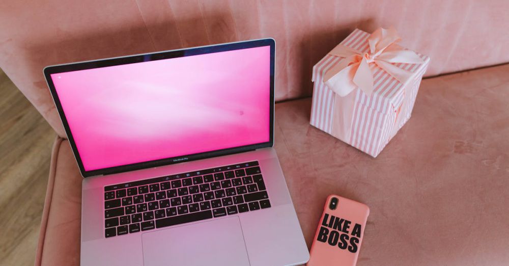 Tech Gifts - A modern workspace featuring a pink-themed laptop, a gift box, and a phone on a pink sofa.