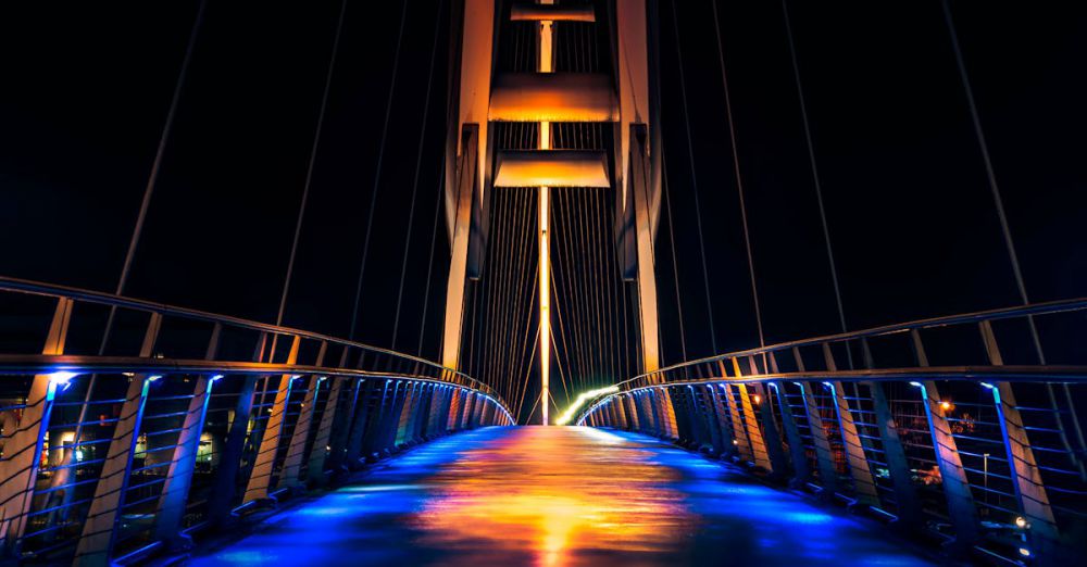 Scenic Zip Lining - Vibrant night view of a modern illuminated bridge with colorful lighting and reflections.