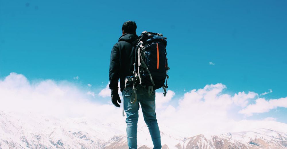 Traveler - A lone hiker with a backpack surveys snow-capped mountains under a clear blue sky.