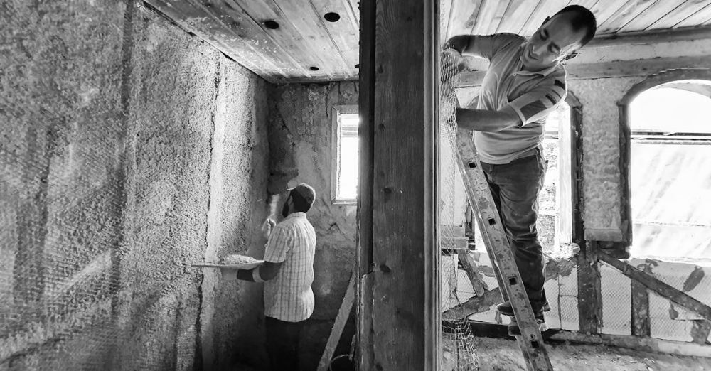 Team Building Zip Lining - Two men renovating a room, one on a ladder applying plaster, showcasing teamwork and effort.