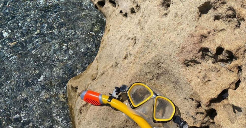 Coastal Zip Lining - Yellow snorkel mask resting on a rock by the clear sea water.