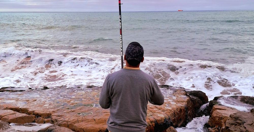 Fishing Gear - A man fishes on the rocky shore of Mar del Plata, Argentina, during a cloudy day.