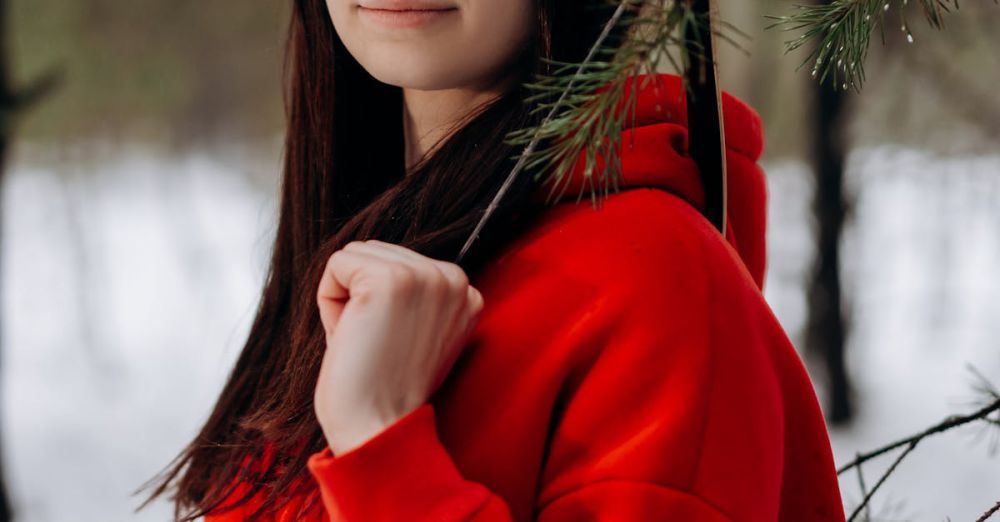 Family Hunting - Portrait of a young woman in a red hoodie holding a bow in a snowy forest setting.