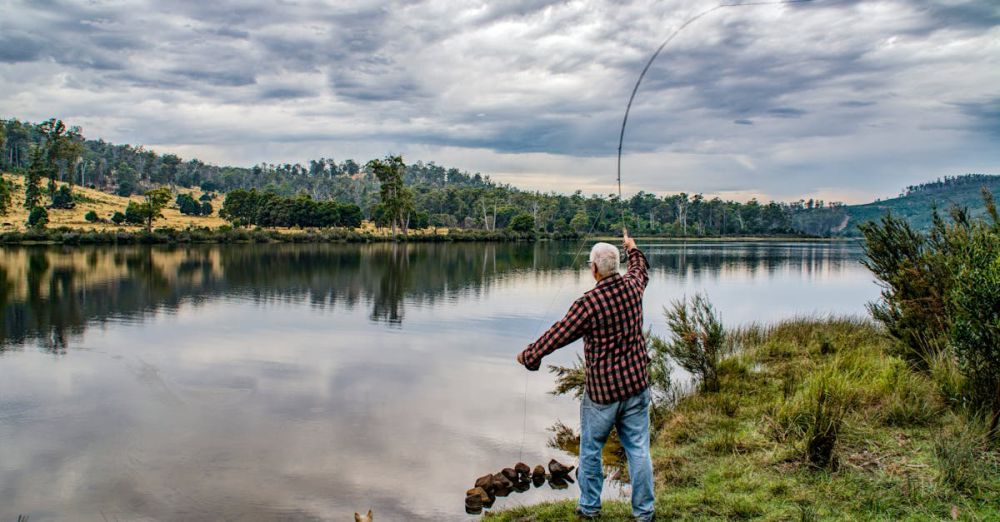 Fly Fishing - Elderly man fishing by a picturesque lake in Ouse, Tasmania, with a dog by his side.