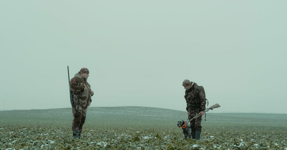 Small Game Hunting - Two hunters with rifles and a dog in a snowy countryside field.