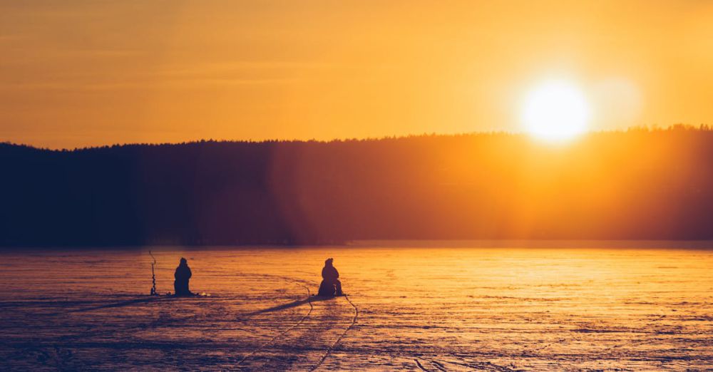 Ice Fishing - Silhouetted figures ice fishing on a frozen lake during a vibrant sunset in Lahti, Finland.