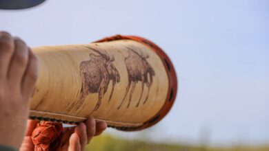 Moose Hunting - Close-up of a person holding a handcrafted moose-decorated horn outdoors against the sky.