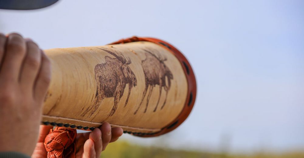 Moose Hunting - Close-up of a person holding a handcrafted moose-decorated horn outdoors against the sky.