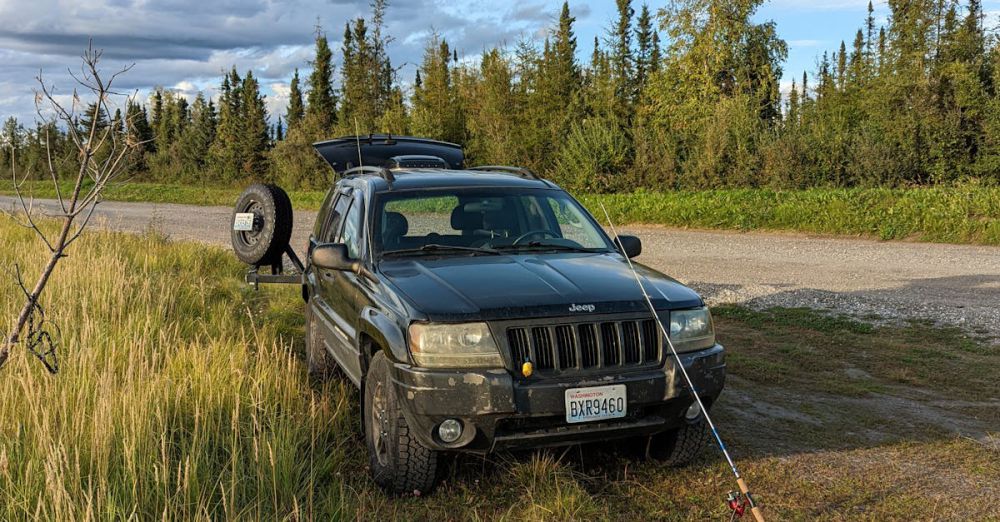 Northern Pike Fishing - Black Jeep parked in grassy area of Alaska with a fishing rod.