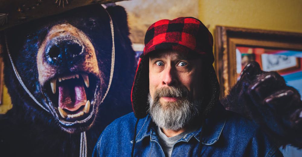 Bear Hunting - A bearded man looking surprised beside a bear mount in a cozy indoor environment.