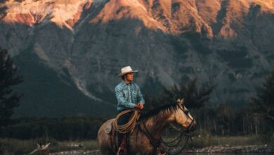 Scenic Views Horseback Riding - A cowboy rides his horse across a scenic river in Waterton Park, Canada with mountainous backdrop.