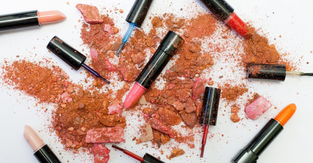 Beauty Products - Colorful scattered makeup products including lipsticks and crushed powders on a white background.