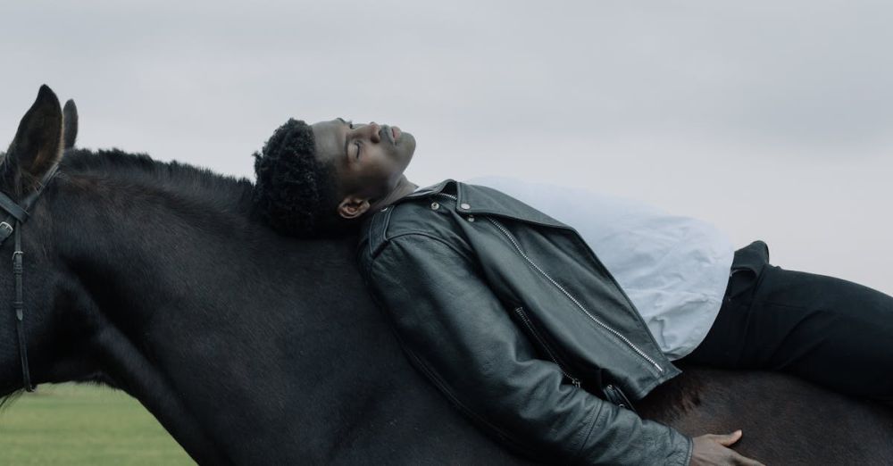 Solo Horseback Riding - A man in a leather jacket lies peacefully on a horse in an open grassy field.