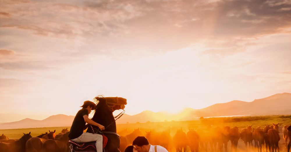 Couple Horseback Riding - A romantic scene depicting a couple embracing with a cowboy on horseback amidst a herd at sunset in Türkiye.