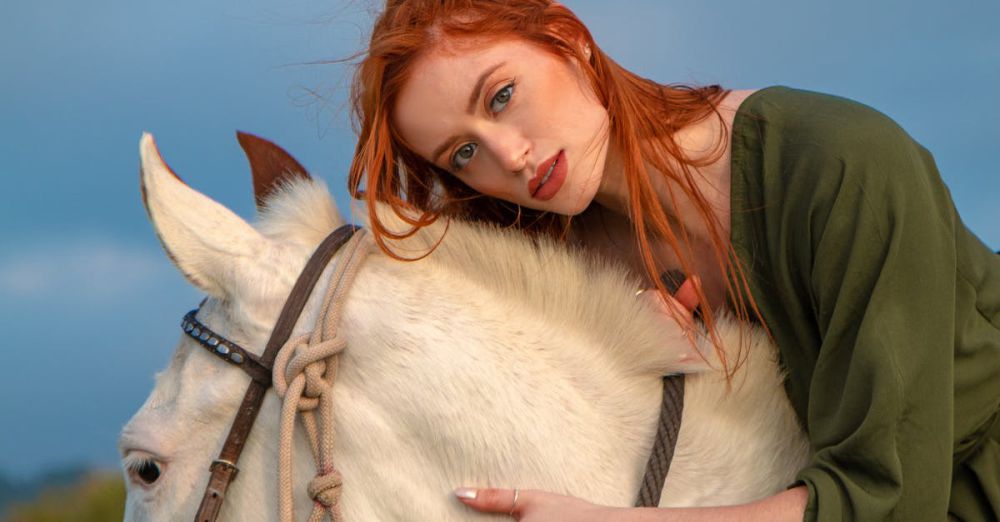 Horseback Riding Photography - A redheaded woman in a green dress poses on a white horse outdoors