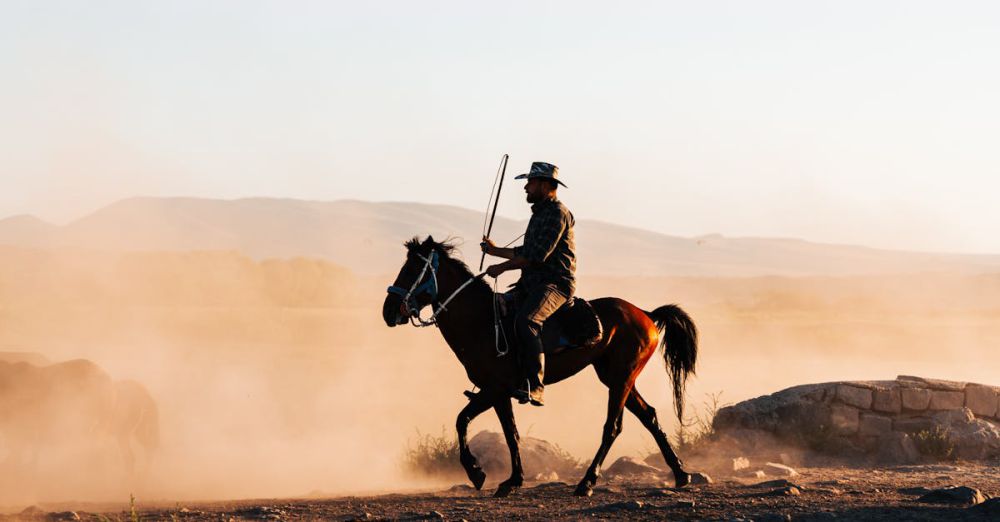 Desert Horseback Riding - A cowboy on horseback traverses a dusty desert terrain at dusk, reflecting wilderness adventure.