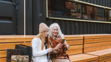 Tech Gifts - Elderly woman with teenage girl enjoying shopping day outdoors, bonding over smartphone.