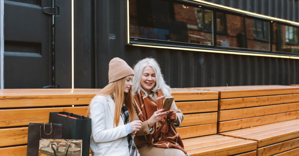 Tech Gifts - Elderly woman with teenage girl enjoying shopping day outdoors, bonding over smartphone.