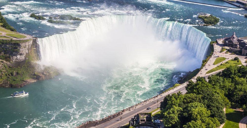 Ontario Waterfalls - Stunning aerial shot of Niagara Falls with a boat tour and lush greenery on a sunny summer day.