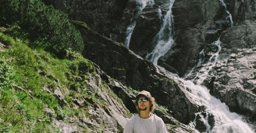 Day Trip Waterfalls - Adventurous man posing by a majestic waterfall on a rocky mountainside during a summer hike.