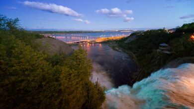 Quebec Waterfalls - A breathtaking view of a waterfall with a distant cityscape and bridge during twilight.