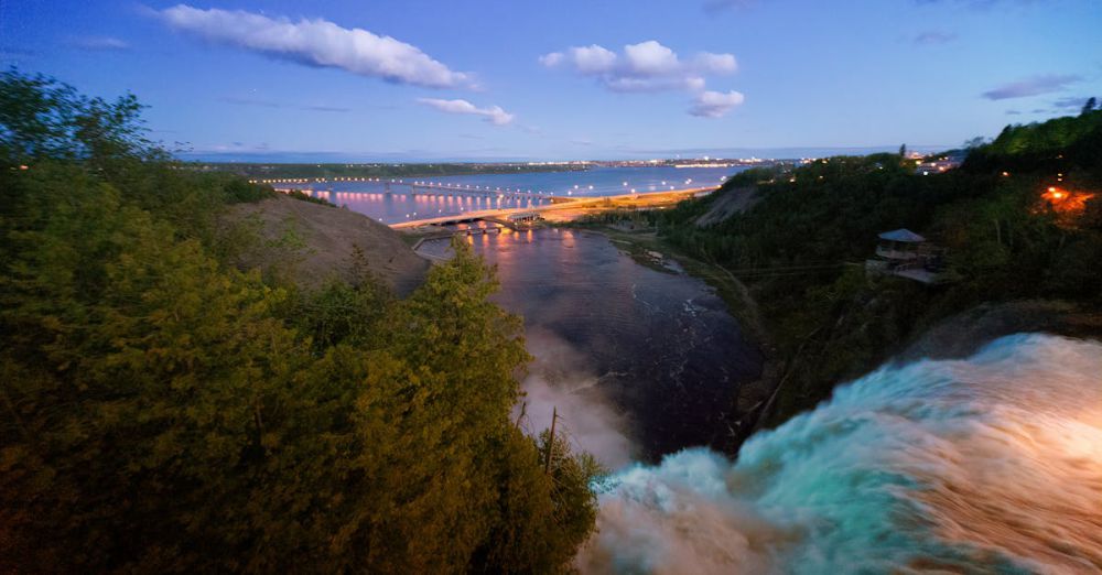 Quebec Waterfalls - A breathtaking view of a waterfall with a distant cityscape and bridge during twilight.