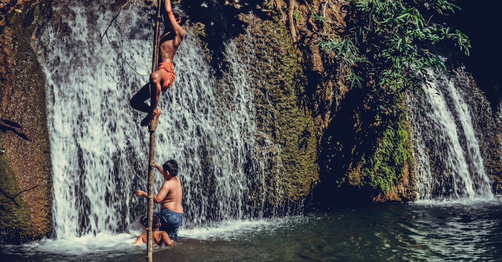 Family Waterfalls - Boys enjoying a summer day climbing near a waterfall in Thailand.